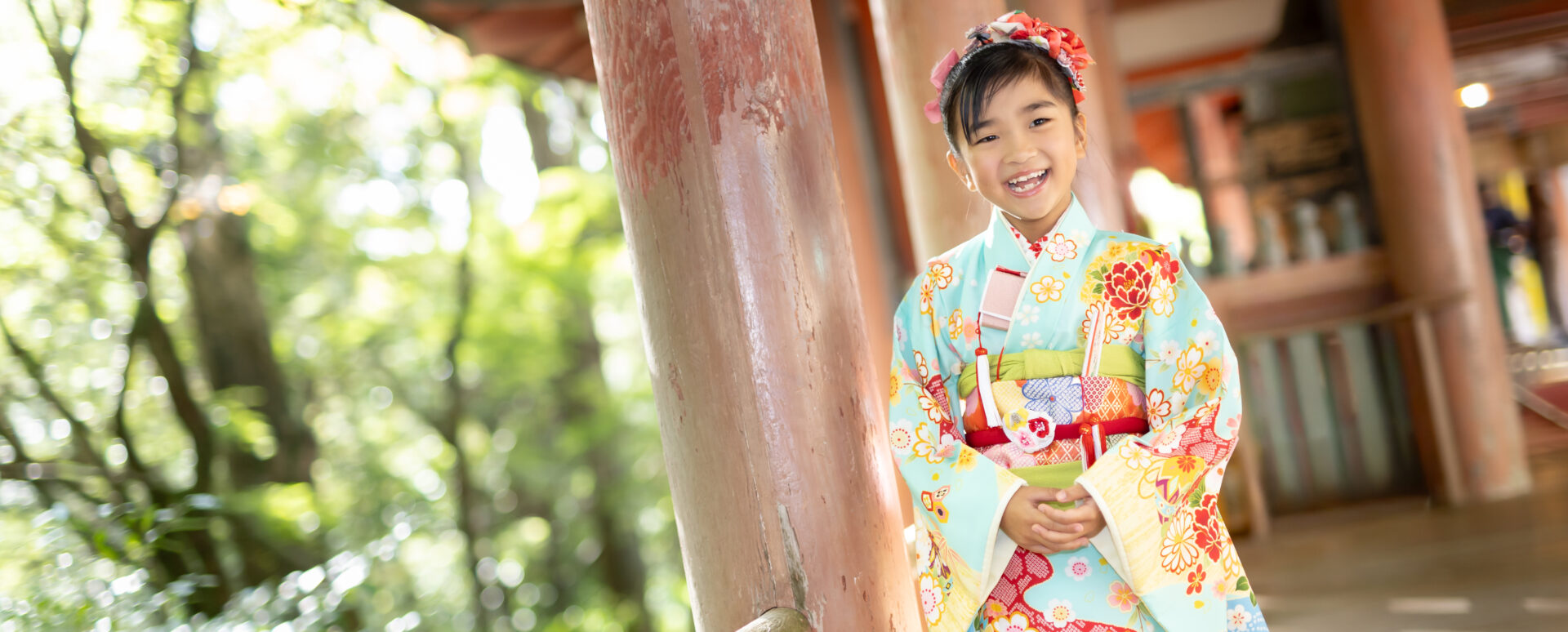大分で七五三の7歳記念撮影。華やかな水色の着物を着て、神社の境内で笑顔を見せる女の子をPhotostudio PASSIONが撮影した七五三ロケーション写真。