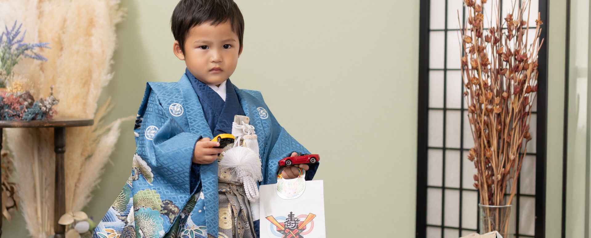 Photostudio PASSIONで、青い着物姿の3歳男の子が大好きなミニカーを手に七五三撮影を楽しむ様子。