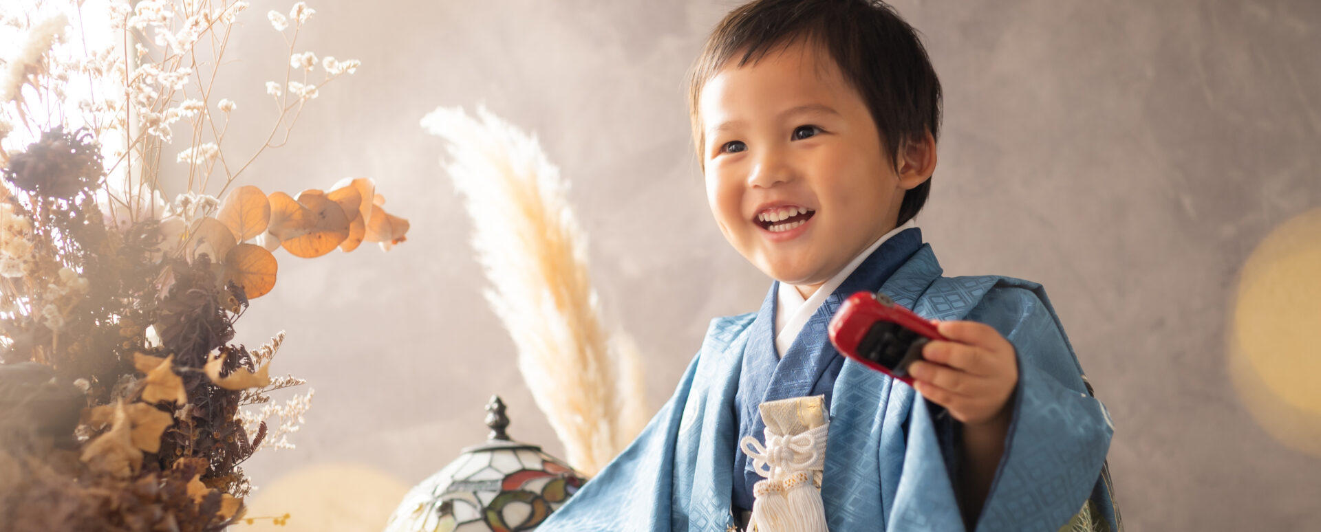 **代替テキスト:**
Photostudio PASSIONで、青い着物姿の3歳男の子がミニカーを手に笑顔を見せる七五三のスタジオ撮影。