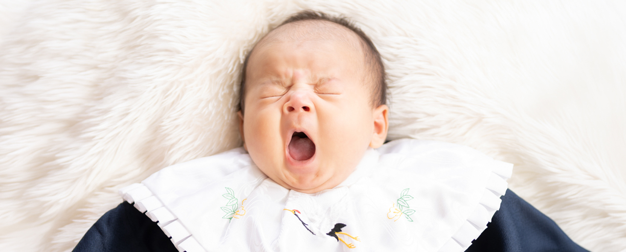**代替テキスト:**
Photostudio PASSIONで、お宮参りの撮影中に大きなあくびをする赤ちゃんの自然な表情を残した記念写真。