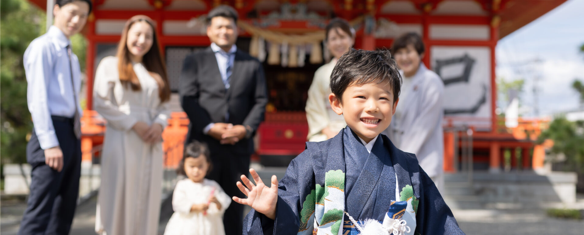 七五三で大分市の若宮八幡宮を訪れた男の子が笑顔で手を振り、後ろで家族が温かく見守る記念写真。