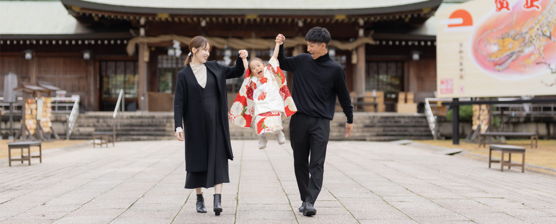 大分市の大分縣護國神社で七五三のお参り撮影をする女の子。パパとママに手をつないでもらい、笑顔で楽しむ家族の記念写真。