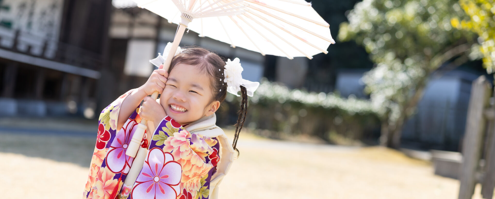大分市の大分縣護國神社で七五三のお参りをする女の子。着物姿で白い和傘を持ち、楽しそうな笑顔を見せる記念写真。