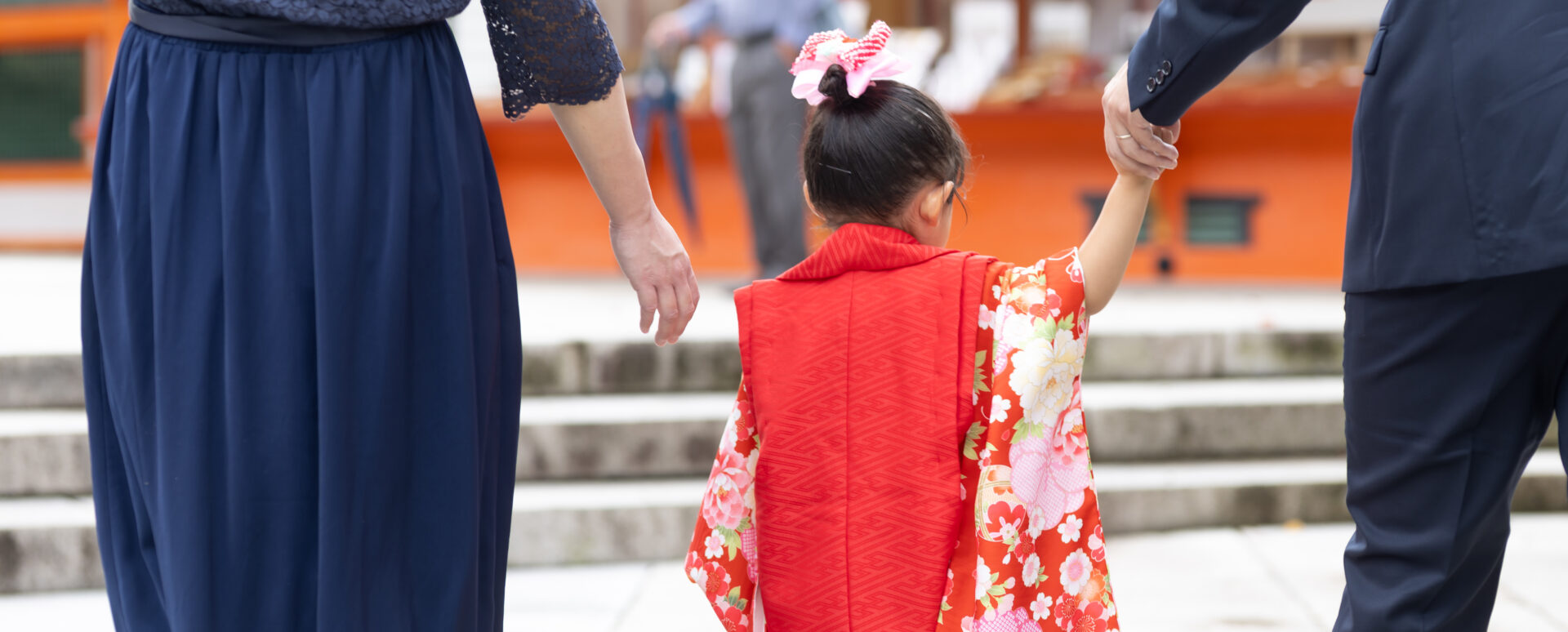 大分県宇佐市・宇佐神宮での七五三。赤い着物姿の女の子がパパと手をつなぎ、境内を歩く後ろ姿。