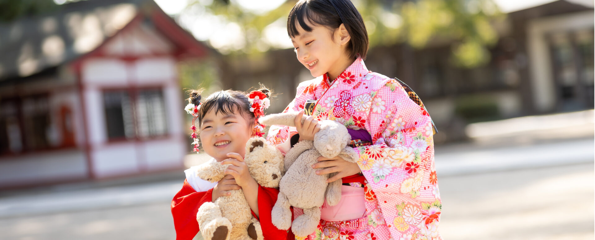 大分県大分市・春日神社での七五三。華やかな着物姿の姉妹がぬいぐるみを抱き、楽しそうに笑い合う様子。