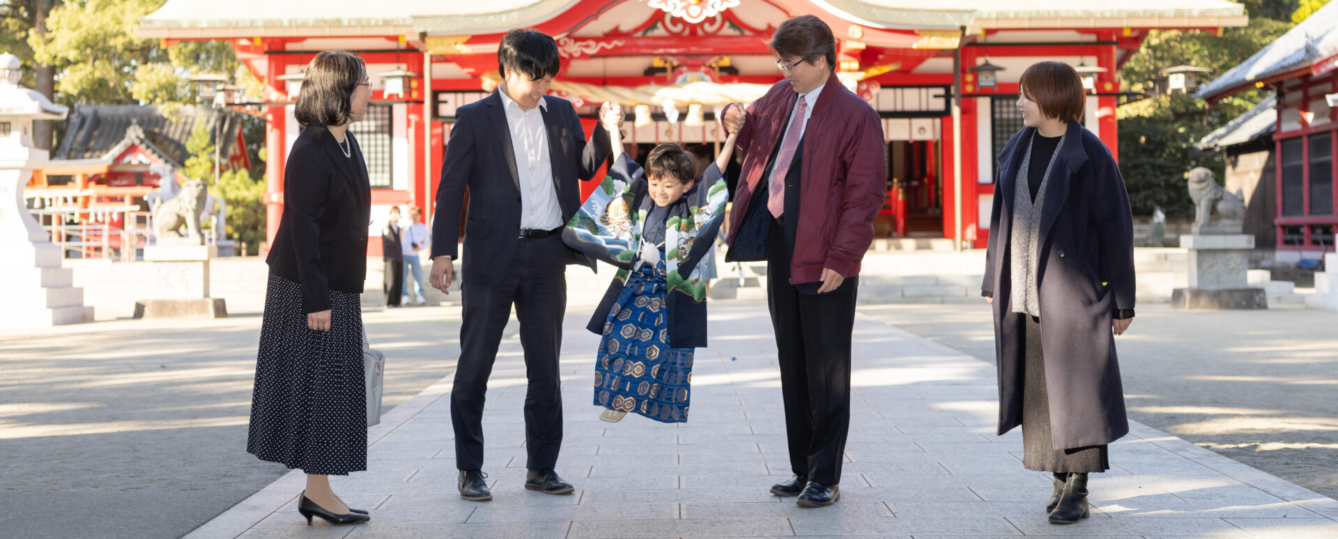 大分県大分市・春日神社での七五三。着物姿の5歳の男の子が家族と手をつなぎ、楽しそうにジャンプする様子。