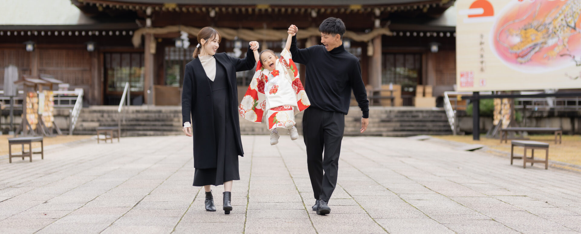 大分県大分市・大分縣護國神社での七五三。着物姿の3歳の女の子が、パパとママに両手をつないでもらい楽しそうにジャンプする様子。