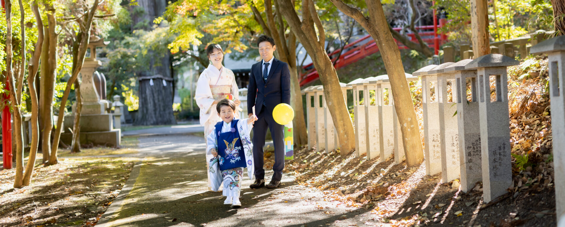 別府市の朝見神社で七五三のお参りをする3歳の男の子。黄色い風船を手に楽しそうに歩き、その後ろをパパと着物姿のママが見守る家族写真。