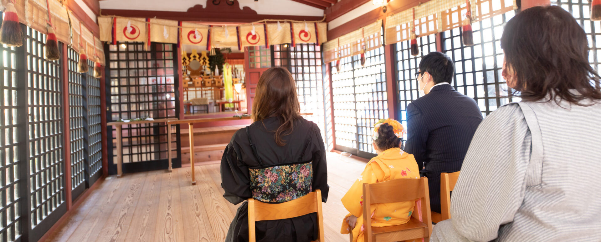 大分県中津市の薦神社で七五三のお参り。オレンジ色の着物姿の3歳の女の子が、パパやママ、家族と一緒にご祈祷を受ける様子。