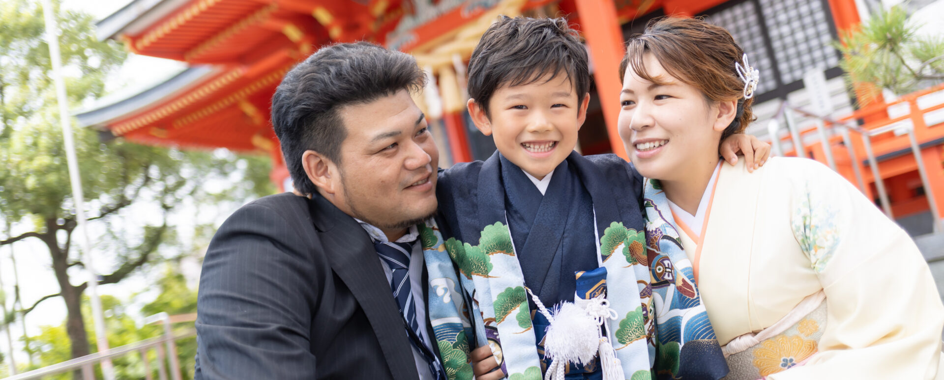 大分市の若宮八幡社で七五三のお参り撮影をする男の子。神社を背景に両親に囲まれ、笑顔を見せる家族写真。