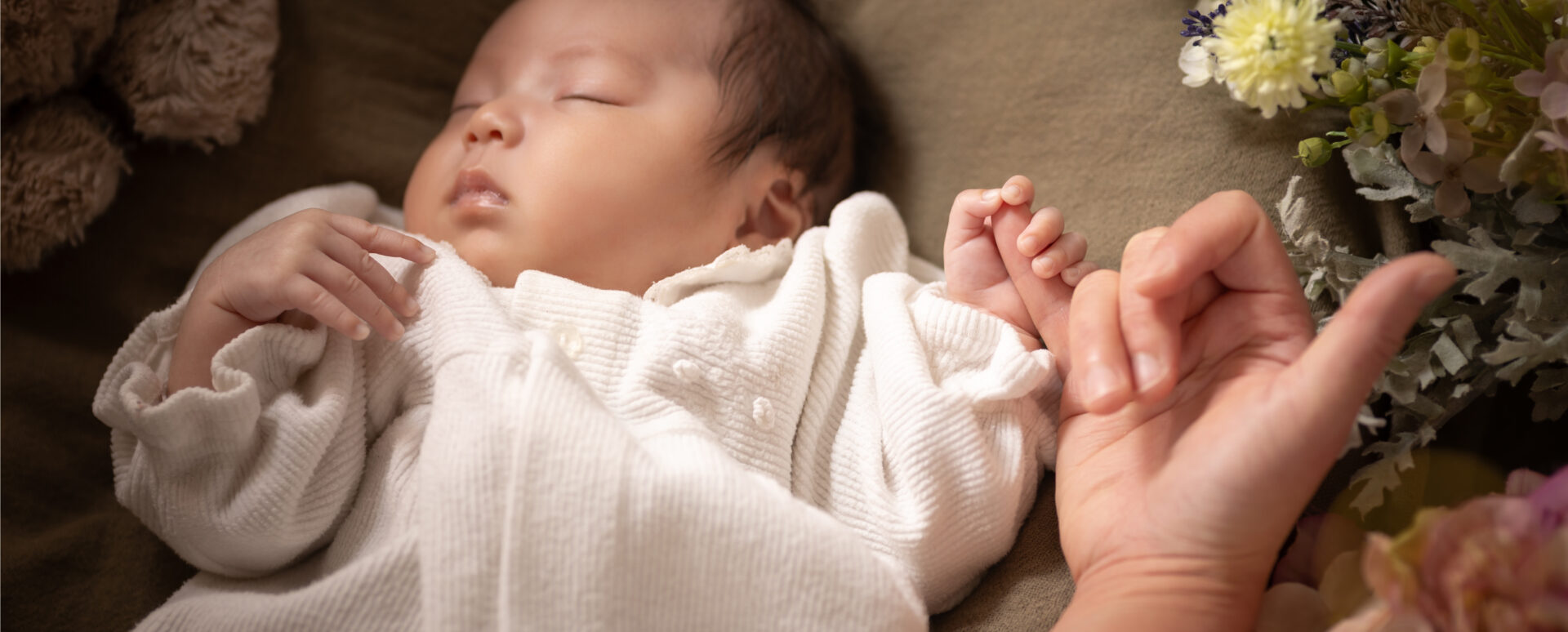 大分のPhotostudio PASSIONで撮影したニューボーン風フォト。眠る赤ちゃんが、お母さんの指を小さな手で握る姿を残した一枚。