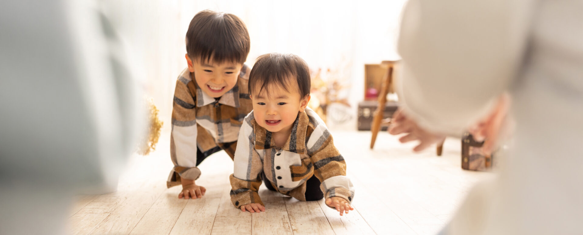 Photostudio PASSION明るくナチュラルなスタジオで、チェック柄のお揃いシャツを着た男の子兄弟がハイハイの姿勢でカメラに向かって顔で見つめ合うキッズ&ベビー写真