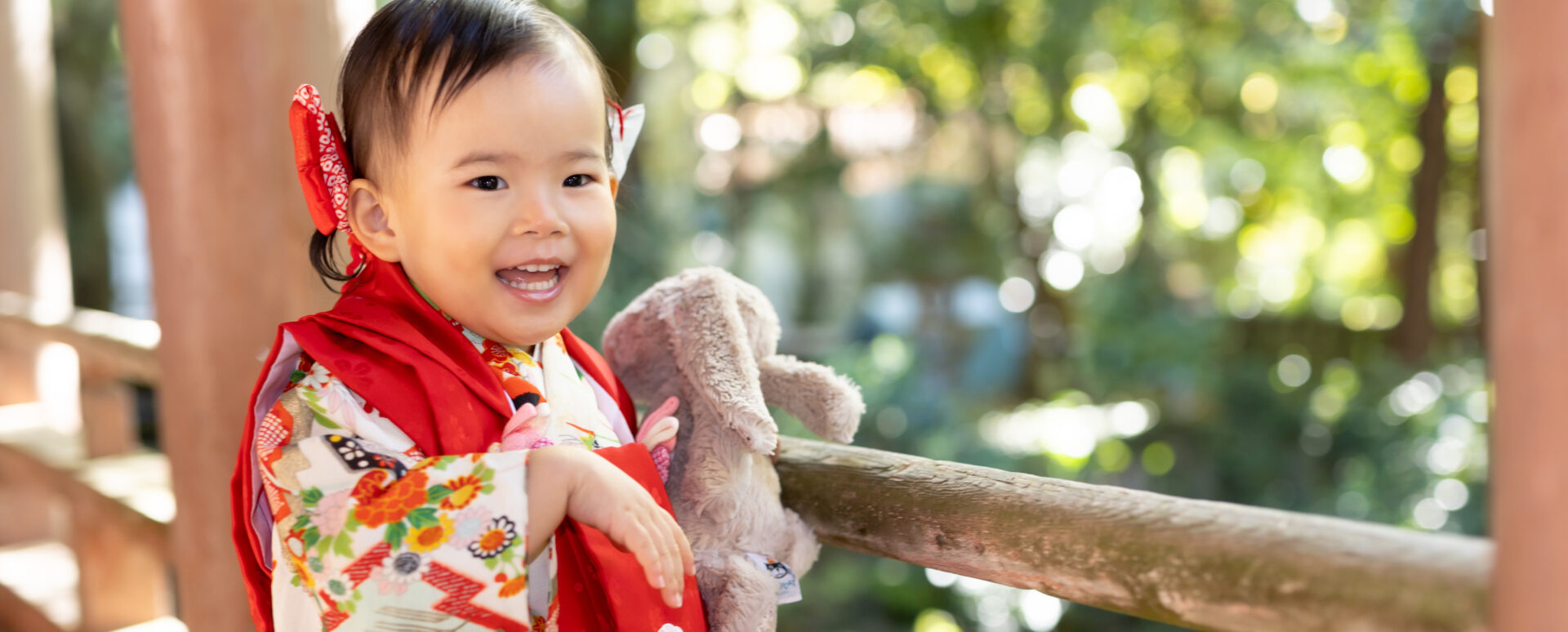 七五三のお参りで、着物姿で大切なうさぎのぬいぐるみと一緒に笑顔を見せる1歳の女の子