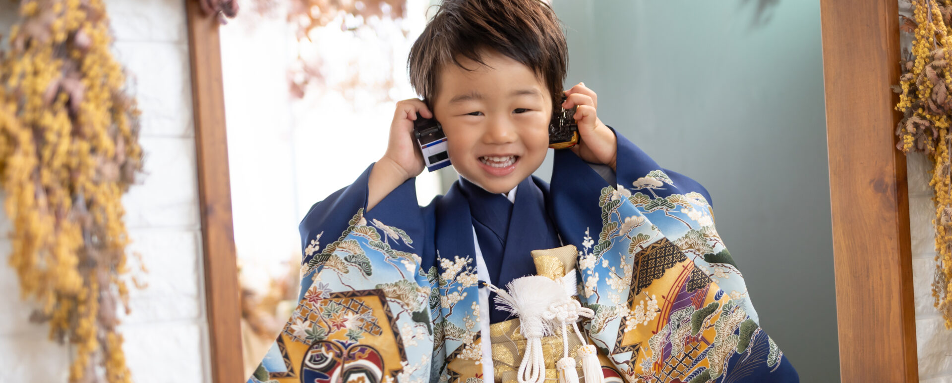 大分のPhotostudio PASSIONで、青い羽織袴姿でおもちゃを耳に当てながら笑顔を見せる3歳七五三のスタジオ撮影