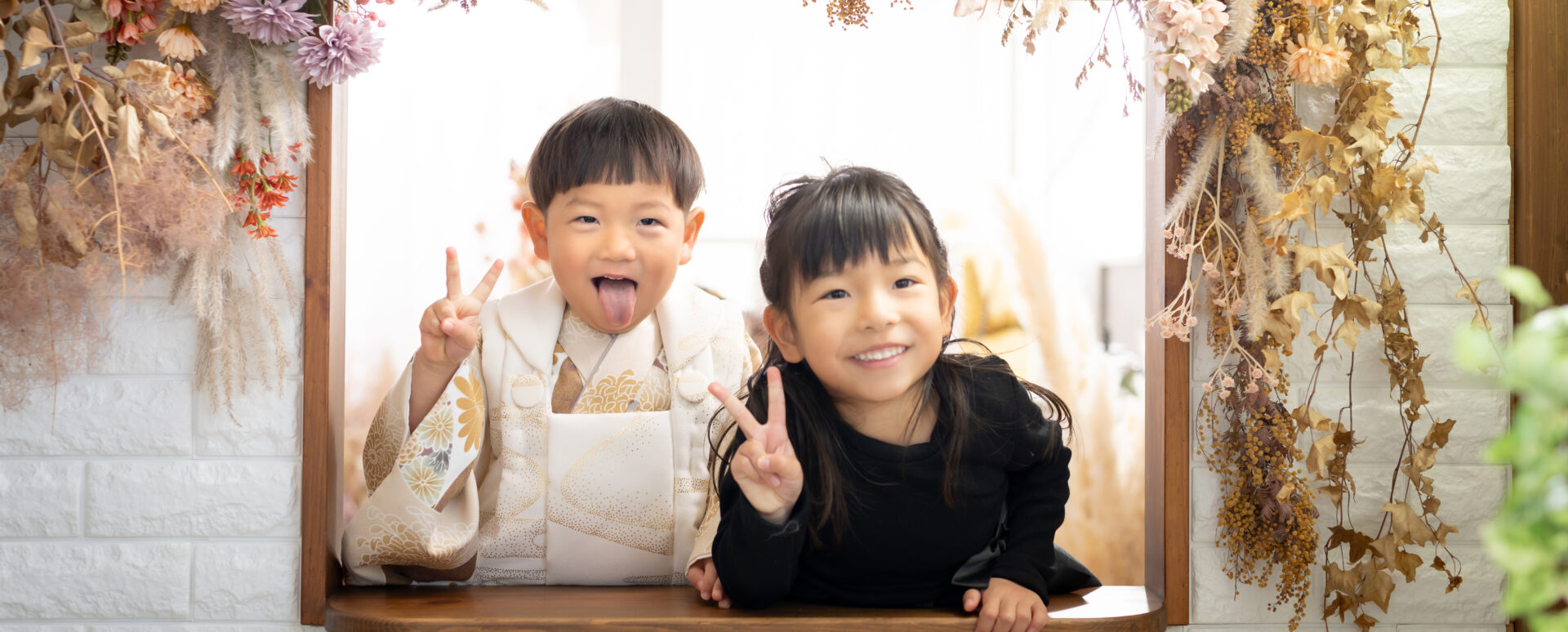 大分のPhotostudio PASSIONで、白い被布姿の3歳七五三の男の子とお姉ちゃんが笑顔でピースするきょうだい写真