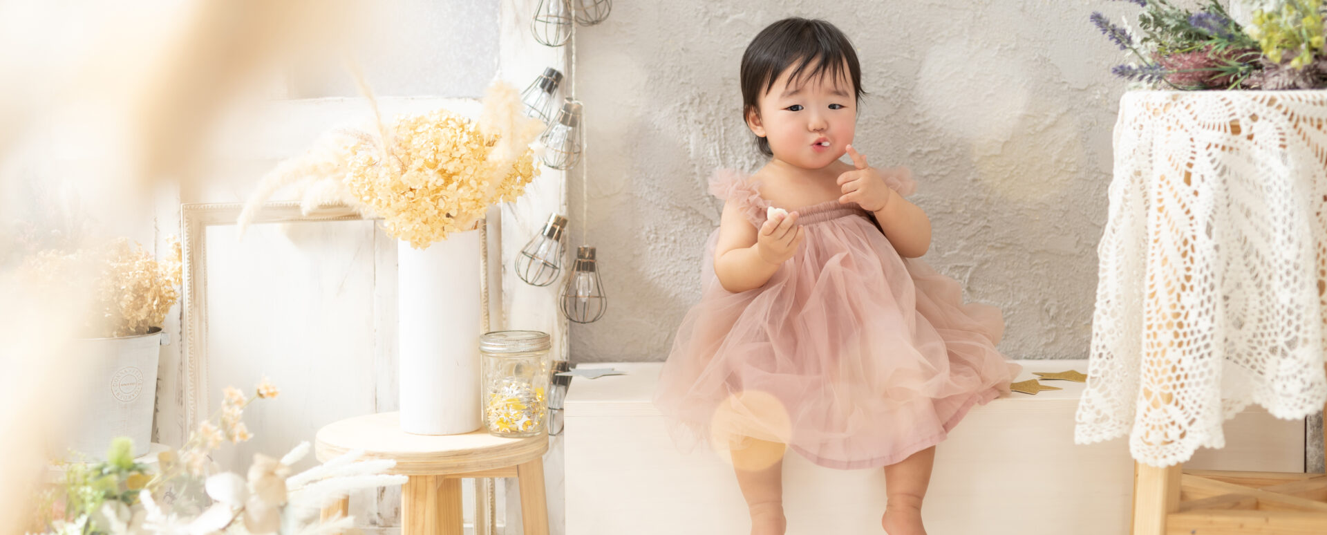 大分のPhotostudio PASSIONで、ピンクのドレス姿でお菓子を食べながら可愛らしい表情を見せる1歳記念のスタジオ撮影
