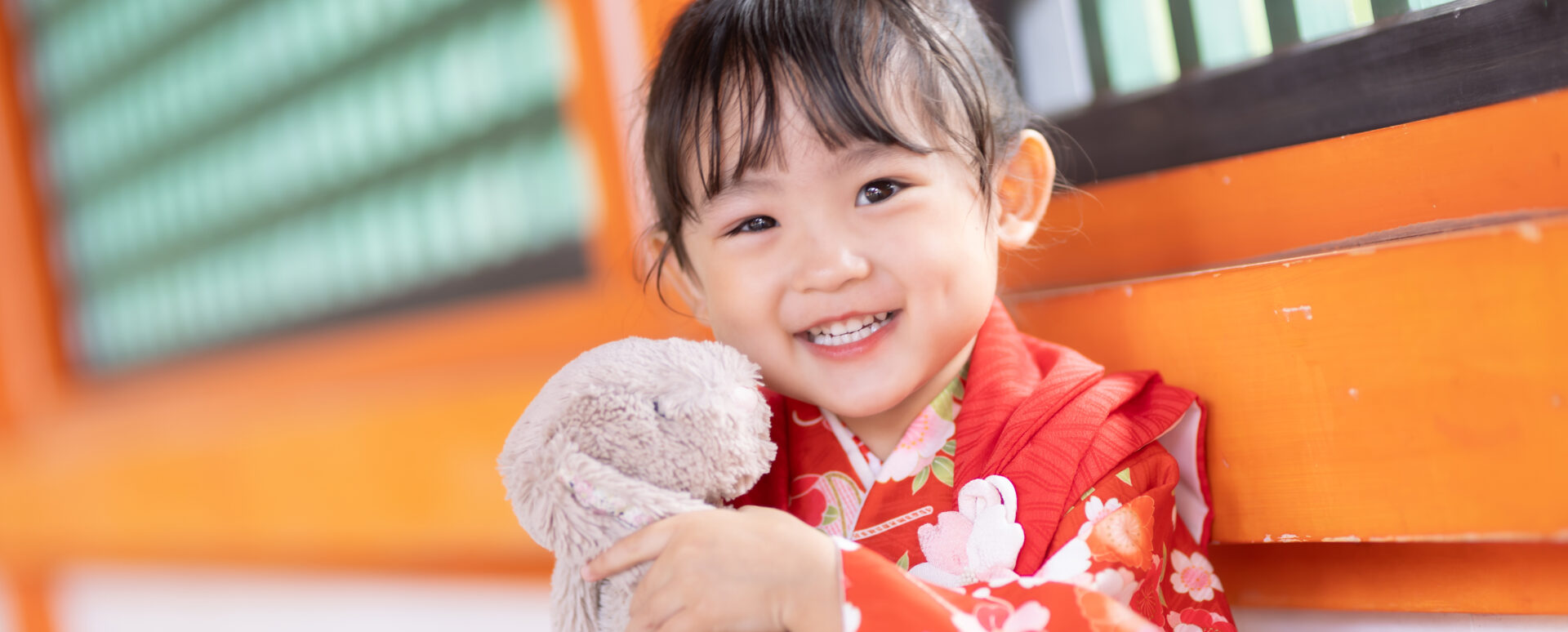 宇佐神宮の七五三のお参りで、赤い着物姿で大切なうさぎのぬいぐるみを抱きしめて笑顔を見せる3歳の女の子