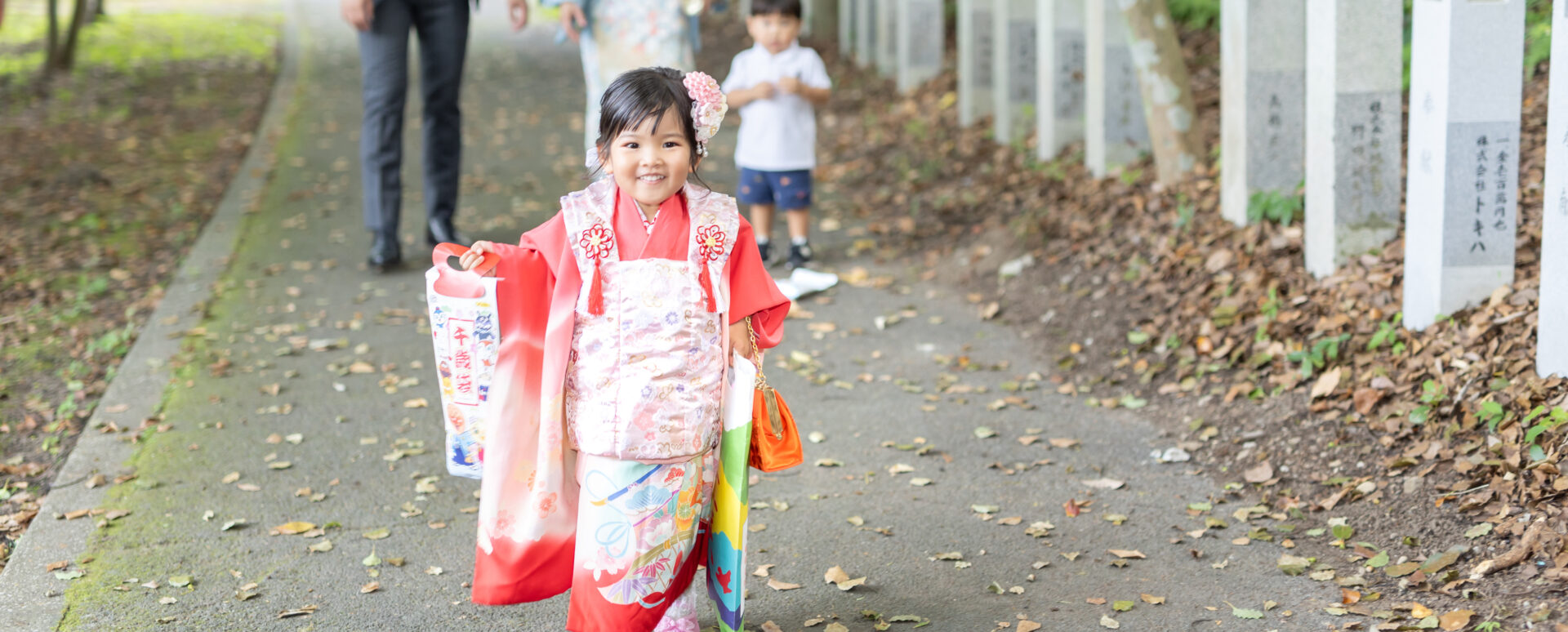 朝見神社の参道で、千歳飴を持ちながら笑顔で歩く華やかな着物姿の3歳七五三のお参り同行撮影
